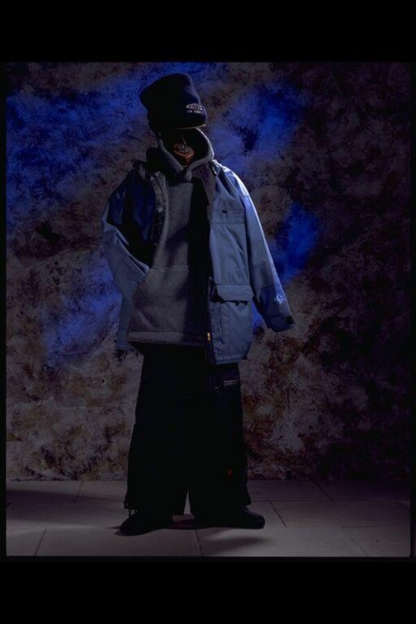 The snowboard outfit: navy fleece beanie, grey fleece pullover under an open blue nylon jacket, wide navy nylon trousers falling over black boots