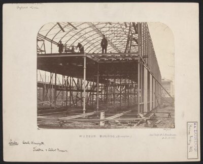 Exterior view of the South Kensington Museum (the 'Brompton Boilers') under construction, looking south with the houses of Cromwell Road and Thurloe Square visible in the background