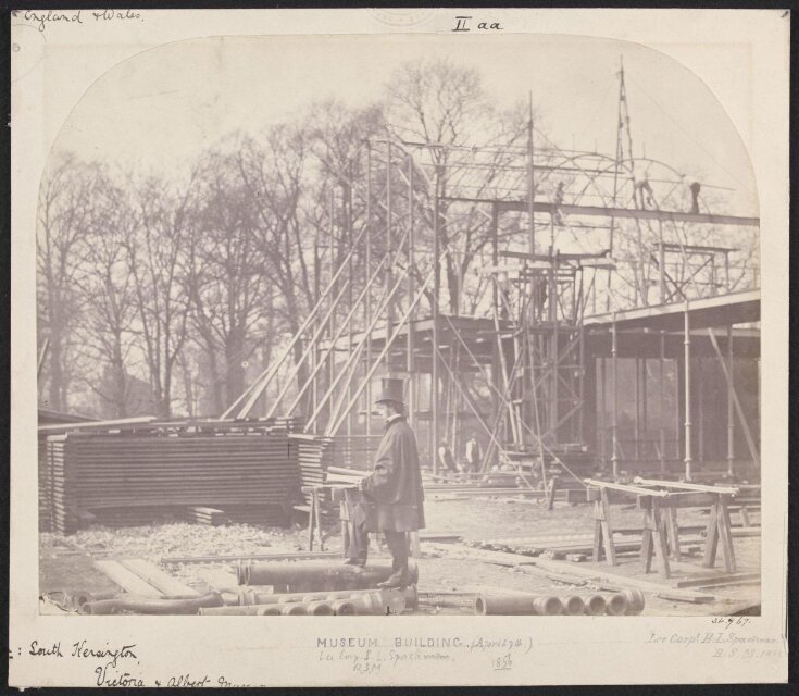 Exterior view of the South Kensington Museum (the 'Brompton Boilers') under construction with B.L. Spackman in the foreground [?] image