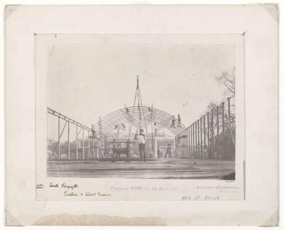 Exterior view of the roof of the South Kensington Museum ('the Brompton Boilers') under construction with the houses of Cromwell Road and Thurloe Square visible in the background