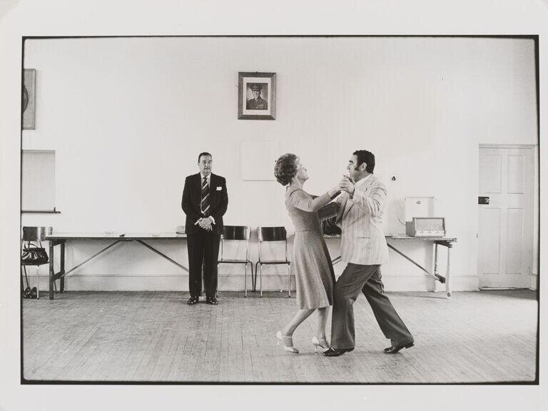 Ballroom dancing teacher, Ted van Rensburg, watches two of his pupils swinging to the music of Victor Sylvester and his orchestra, in the old Court House, Boksburg. by Goldblatt, David