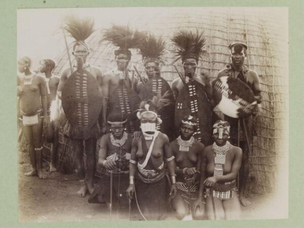 A group portrait of (?) Zulu men and women in tribal dress. They are ...