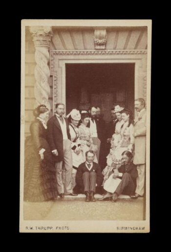 A photograph of 12 people by a door of a building