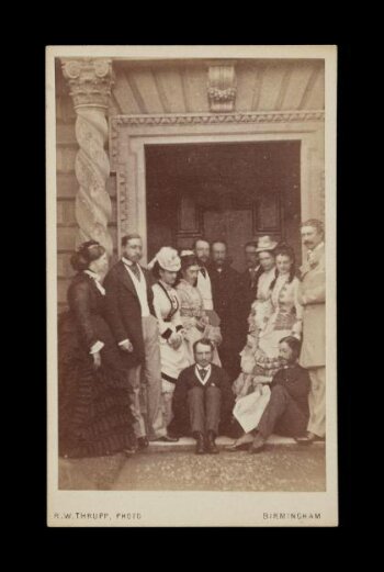 A photograph of 12 people by a door of a building