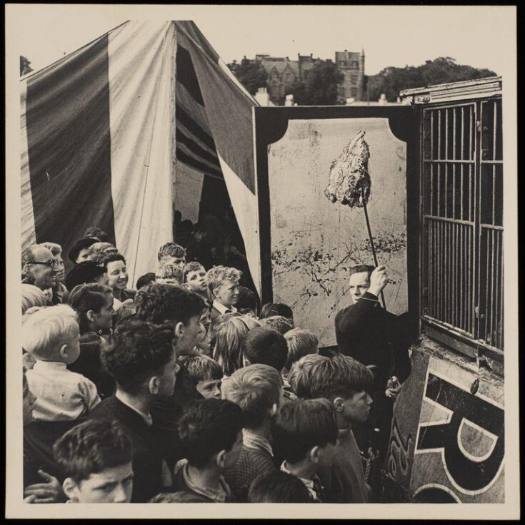 crowd of people standing in front of a cage waiting for an animal to be fed top image